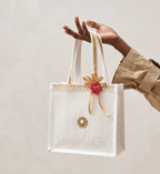 Hand holding a decorative tote bag with a red flower and gold bow on a light background
