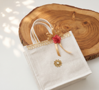 Beige tote bag with gold accents and a red flower on a wooden surface